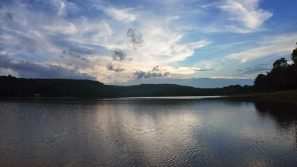 Wall Mural - Sunset's warm glow reflects on the calm lake, nestled amidst majestic mountains under a vast, cloud-streaked sky, showcasing nature's serene beauty