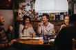 © qunica.com - A group of friends laughing and sharing drinks and food around a cozy table indoors, showcasing warmth, joy, and camaraderie in a relaxed and friendly setting.
