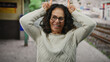 © Krakenimages.com - Woman with curly hair making playful gesture outdoors at a train station, exuding joy and confidence against a railway backdrop, wearing glasses and a cozy sweater.