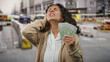 © Krakenimages.com - Woman outdoors in city holding singapore dollars while covering her ear from street noise, depicting a financial and urban lifestyle scene.