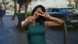 © Krakenimages.com - Woman smiling outdoors making peace sign and pointing at camera on city street during daytime showcasing joyful expression and positive energy.
