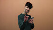 © Krakenimages.com - Young man with phone smiling and pointing at camera over brown background, conveying connection and engagement with audience, showcasing charm and technology use.