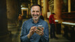© Krakenimages.com - Man smiling while using smartphone inside church with blurred background and column structures visible, capturing a candid moment of joy and technology interaction.