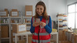 © Krakenimages.com - Young woman volunteer using phone in charity donations center room with boxes in the background showcasing a community support environment indoors.
