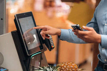 With pineapple. Close up view of man customer that is paying for products by credit card in grocery store