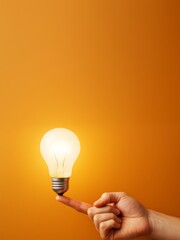 Poster - Hand balancing glowing light bulb on fingertip against orange background as symbol of bright idea and creative business inspiration concept.