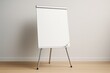 © Pixels Hunter - Blank flip chart easel mockup standing in bright room with wooden floor and neutral wall background for design presentation or branding concept.