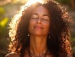 © Shelley - Woman with curly hair smiling with closed eyes in sunrise sunlight, practicing yoga outdoors, deep breathing, wearing a necklace, enjoying nature.