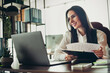© deagreez - Confident businesswoman working in an office holding documents and smiling while sitting in professional workspace setting