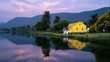 © fotofabrika - Beautiful yellow house by the calm lake at dusk surrounded by mountains and vibrant greenery