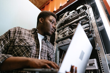 Poster - IT professional manages server rack while working on laptop in a data center during afternoon hours