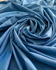 blue fabric is arranged in a spiral pattern with soft folds and smooth texture