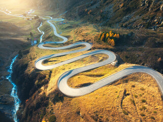 Wall Mural - aerial view of winding mountain road, river in alpine valley at sunrise in autumn. top view of road 