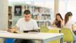 © JackF - European guy is sitting at a table, reading a book and making notes in a notebook, he is preparing to enter the university in the new academic year. Students study in the library