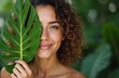 © Vadym - Beautiful natural woman covers face with large tropical leaf. Smiling girl enjoys wellness, spa treatment. Skin care, body care concept with palm leaf. Happy, healthy, pure, young woman shows organic