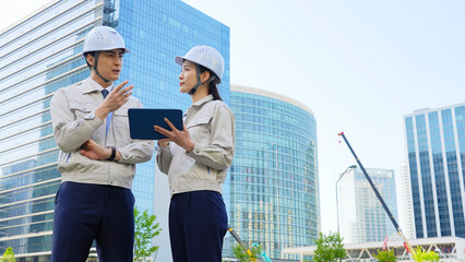Poster - 建設現場でタブレットを見ながら打ち合わせする男女エンジニアのグループ
