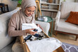 © Jovo Jovanovic/Stocksy - Happy woman in hijab unboxing beauty cosmetics while sitting on sofa