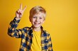 © Vadym - Happy little boy shows victory gesture on yellow background. Smiling kid wearing shirt. Cheerful young male model shows peace fingers symbol. Kid facial expression. Positive emotions, childhood.