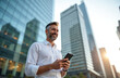 © Vadym - Smiling professional man holding smartphone, enjoying business lifestyle in financial district. Happy entrepreneur using mobile phone smiling at urban setting, downtown. Successful, confident,