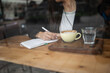 © Lupe Rodriguez/Stocksy - Young woman writing in diary at café