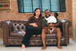 © chokniti - Heartwarming family moment as an African American father and daughter share playful time together on the couch, surrounded by love, laughter, and the warmth of home, while mom gently looks on with joy