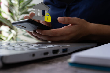 Poster - A person holding a smartphone with the symbols of a bank and a padlock on it, sitting at an office desk near a laptop. Bank security concept.