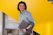 © VICTOR TORRES/Stocksy - Smiling professional with laptop against yellow backdrop