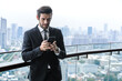 © Jack Tamrong - Handsome male executive businessman using phone in office balcony with blurred skyscraper downtown view