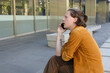 © Rowena Naylor/Stocksy - Young man talking on phone while sitting outside modern building