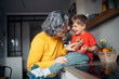 © Santi Nuñez/Stocksy - Grandmother and grandson sharing a laugh in the kitchen