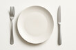 © Shakhnoza - White plate with fork and knife on a wooden table, set for an elegant dinner.