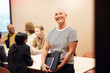 © Johnér - Portrait of happy short haired businesswoman holding laptop and diary while standing in office meeting room