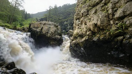 Poster - A powerful waterfall cascades through rocky cliffs surrounded by lush greenery in a natural wilderness setting.