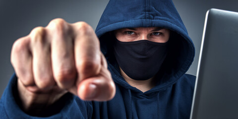 Aufkleber - Close-up of fist and masked person in hoodie, laptop in background, symbolizing online threat, aggression, or cybercrime