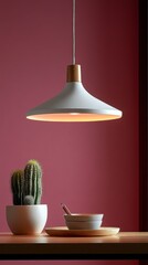 Poster - In a stylish dining space, a modern pendant light casts a warm glow above a wooden table. A ceramic bowl and polished utensils sit next to a potted cactus, creating a serene ambiance