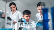 © Irin - Three young scientists in lab coats collaborate on a research project using a microscope and taking notes, surrounded by lab equipment and blue liquids, showing teamwork and scientific analysis.