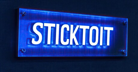 Aufkleber - Bright blue sign displays STICKTOIT text. Illuminated lettering contrasts dark background. Modern design, simple presentation.