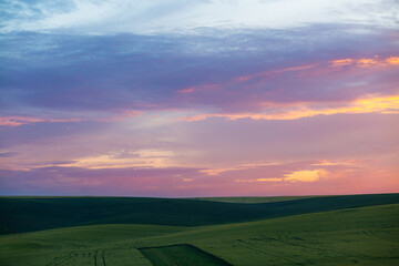 Poster - Vibrant sunset casts a magical glow over rolling green hills in a serene landscape.