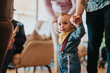 © qunica.com - A young toddler is learning to walk with the guidance of two adults inside a comfortable home setting, conveying family moments and developmental milestones.