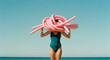 © Uncanny Valley - Woman in swimsuit concealing face with pink pool noodles at the beach