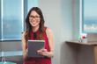 © WavebreakMediaMicro - Adult woman wearing polka dot blouse and eyeglasses holding tablet at office desk by large windows