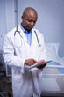 © WavebreakMediaMicro - African American male physician reviewing tablet in hospital room with stethoscope and bed linens
