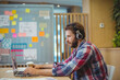 © WavebreakMediaMicro - Man wearing plaid shirt and headphones working on laptop at office near sticky notes, copy space