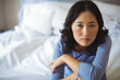 © WavebreakMediaMicro - Asian woman sitting on bed with white pillows and sheets folding arms and looking serious