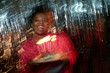 © Seventyfour - Portrait of Black woman smiling while holding birthday cake with lit candles, celebrating birthday, looking at camera with festive blurred lights in background