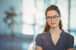 © WavebreakMediaMicro - Woman wearing eyeglasses and navy polka-dot blouse standing in coworking space with potted plant