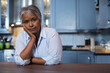 © wavebreak3 - Senior African American woman leaning on wood countertop in kitchen observing shaker-style cabinets