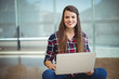 © WavebreakMediaMicro - Woman wearing plaid shirt and jeans sitting on polished floor in study lounge using silver laptop