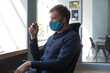 © WavebreakMediaMicro - Man in 30s in office chair wearing blue face mask, holding pen and gazing out window