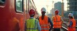 © Viktor - Construction workers observe red train at railway site. Teamwork, safety in transportation infrastructure, men at work wearing safety vests and helmets. Urban environment, train track.